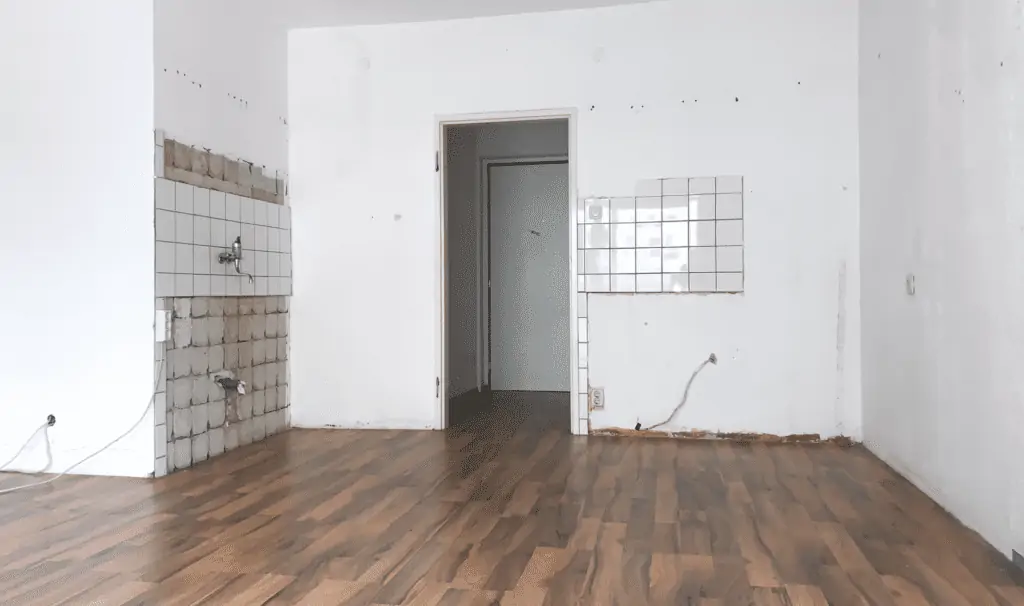 Eine unrenovierte Wohnküche mit braunem Boden und weißen, beschädigten Fliesen